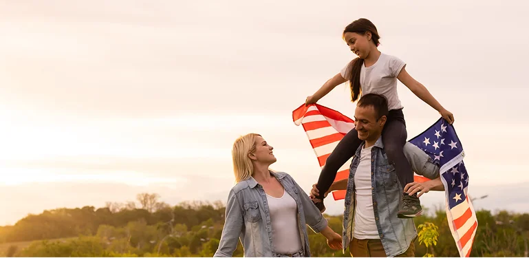 A family proudly drapes an American flag over their shoulders, smiling together in a show of patriotism.