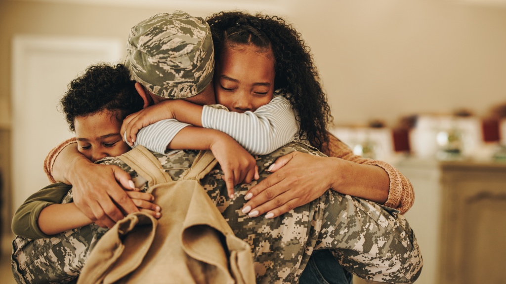 Military parent hugging his children