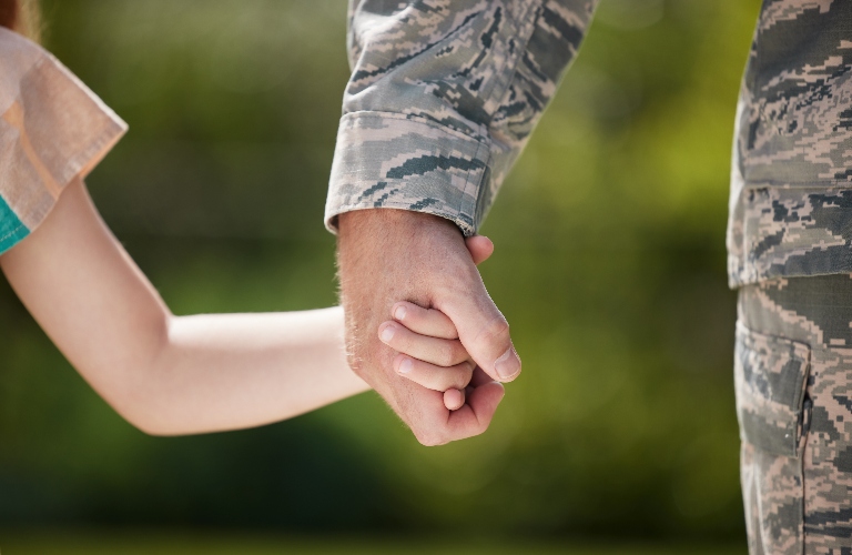 Military man holding his daughters hand outside