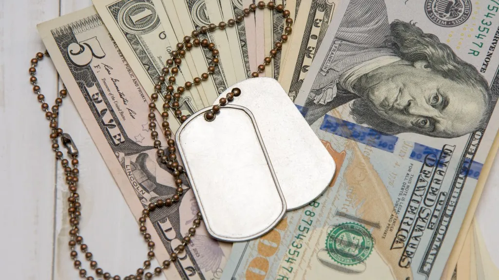 An army medallion rests on a hundred dollar bill