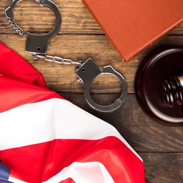 A U.S. flag drapes over a wooden surface alongside handcuffs and a gavel, symbolizing law and justice.