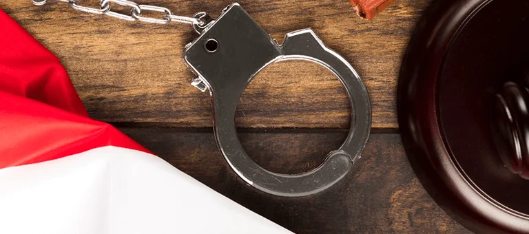 A U.S. flag drapes over a wooden surface alongside handcuffs and a gavel, symbolizing law and justice.