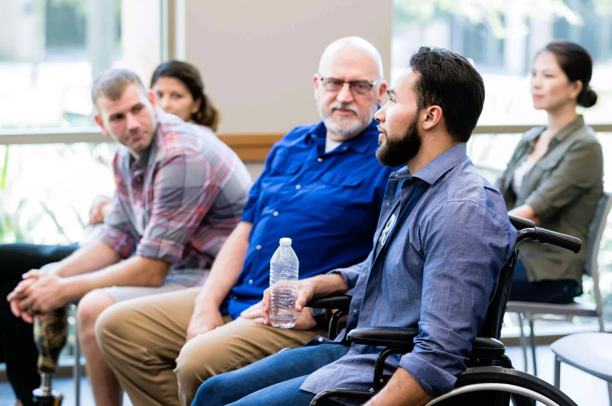 Diverse group of people, including a man in a wheelchair, attending a support group meeting.