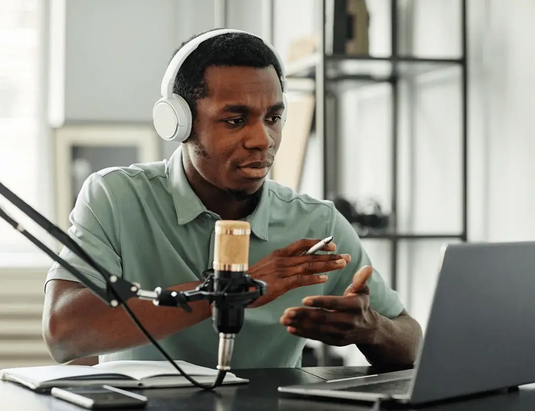 A man wearing headphones speaks into a laptop, engaged in a conversation.