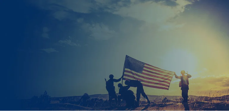 A group of people stands on a hill, proudly holding an American flag against a clear blue sky.