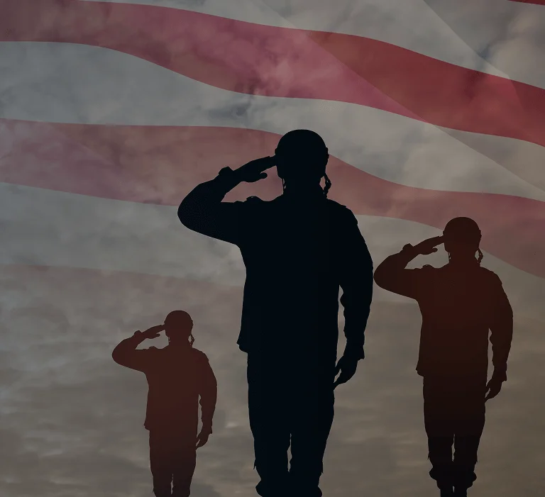 Silhouettes of three soldiers saluting against a backdrop of the American flag and a cloudy sky, symbolizing honor and patriotism.