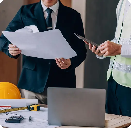 Two construction managers review blueprints and a tablet on-site