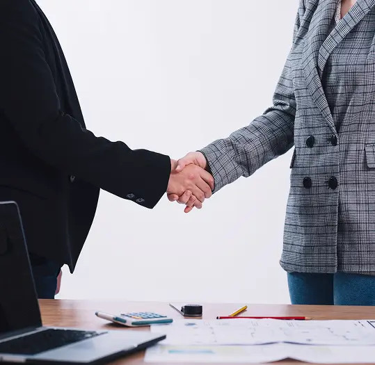Two people shaking hands over a desk with office supplies
