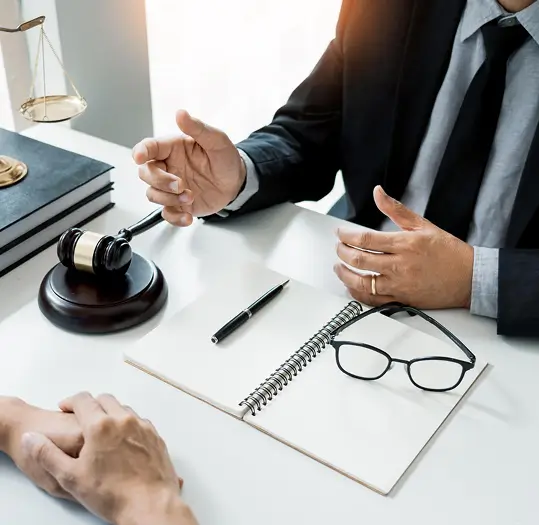 Lawyer in suit consults with client at desk with gavel, scales of justice, and notebook.